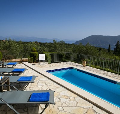 Sun loungers and pool with views from the terrave of the coastline and mountains of Kefalonia, Greek Islands